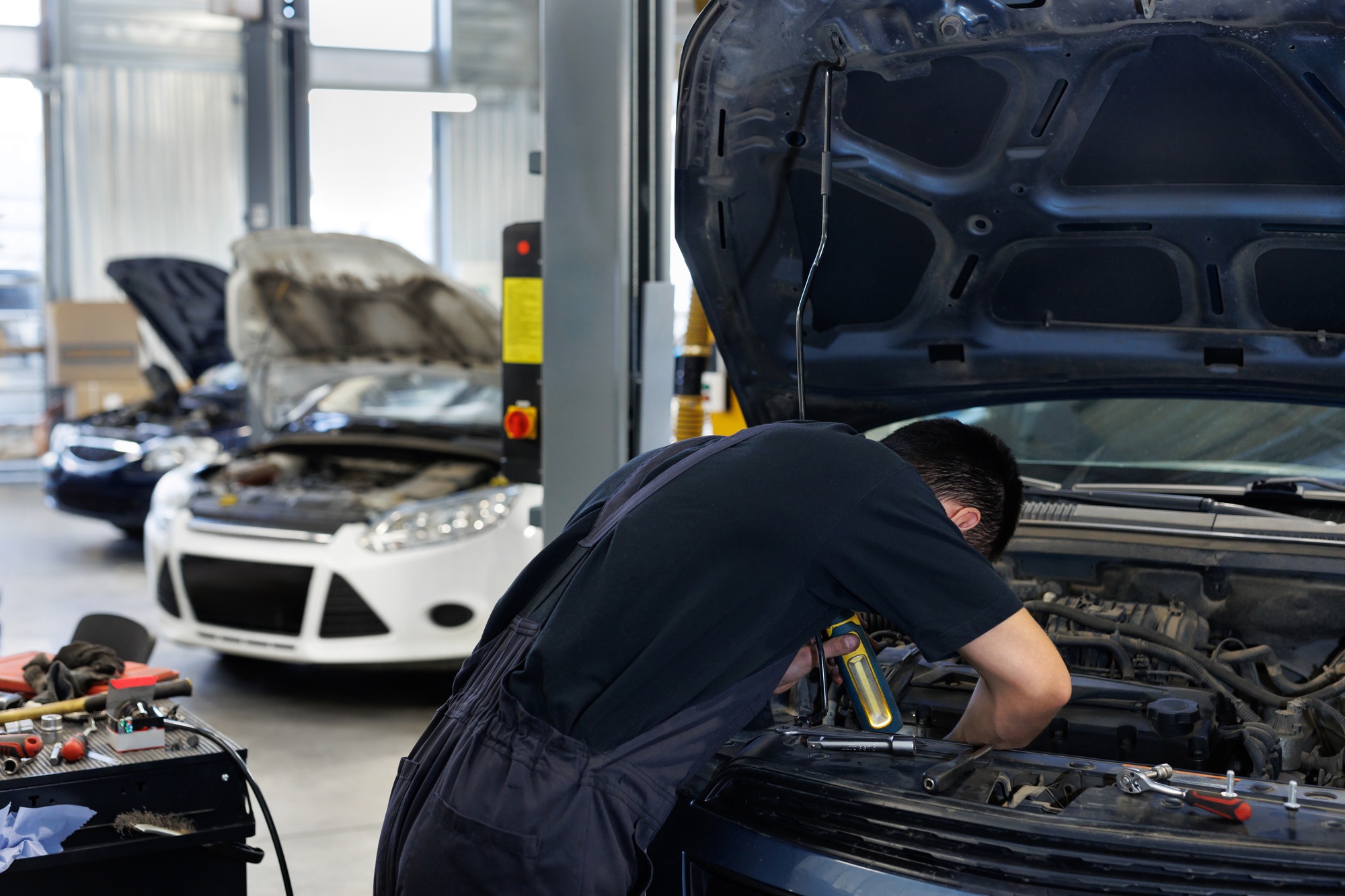 Close-up of a worker, a repairman, repairing a car. The open hood of the car in the repair garage.